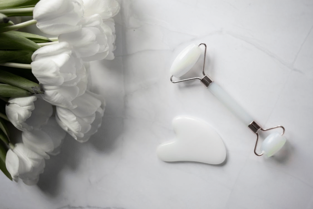An image of skincare tools placed on a marble surface next to some white flowers