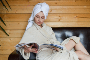 A woman in a bathrobe reading a magazine inside a wooden sauna room.