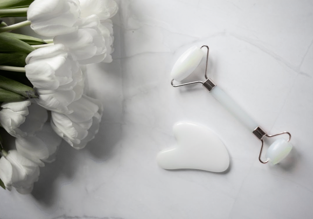 An image of skincare tools placed on a marble surface next to some white flowers