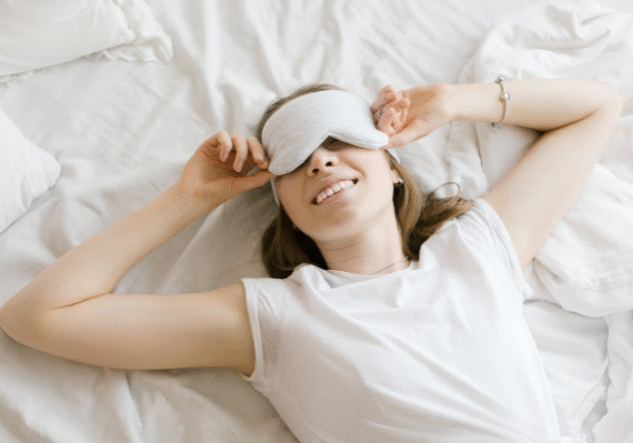 A young woman lying in bed with an eye mask, smiling and appearing relaxed.
